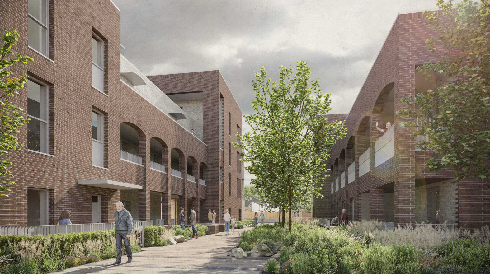 Image shows people walking on a paved pathway through grass, flowers and trees between two brick buildings with balconies.