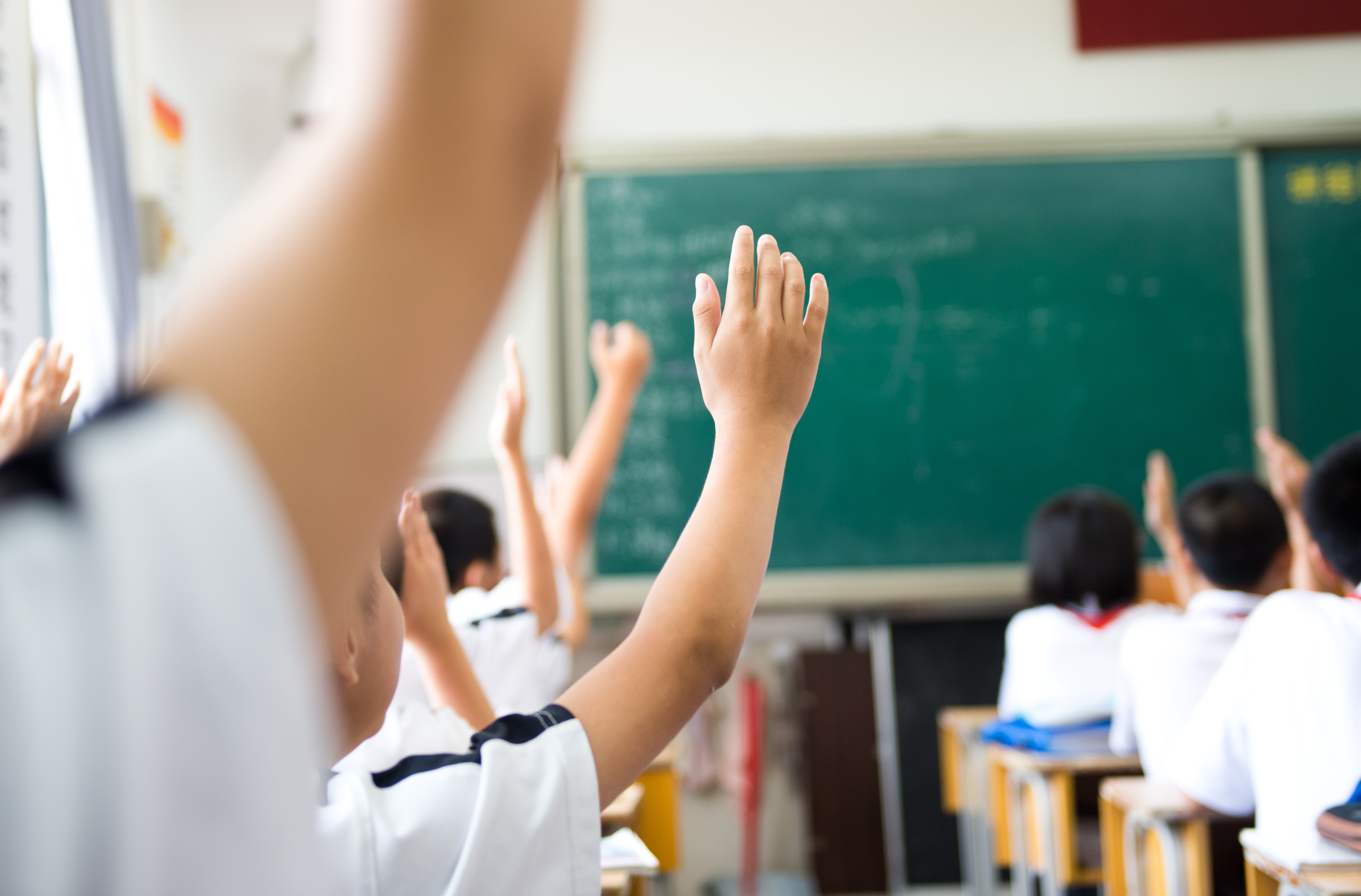 Secondary school pupils with their hands up in class