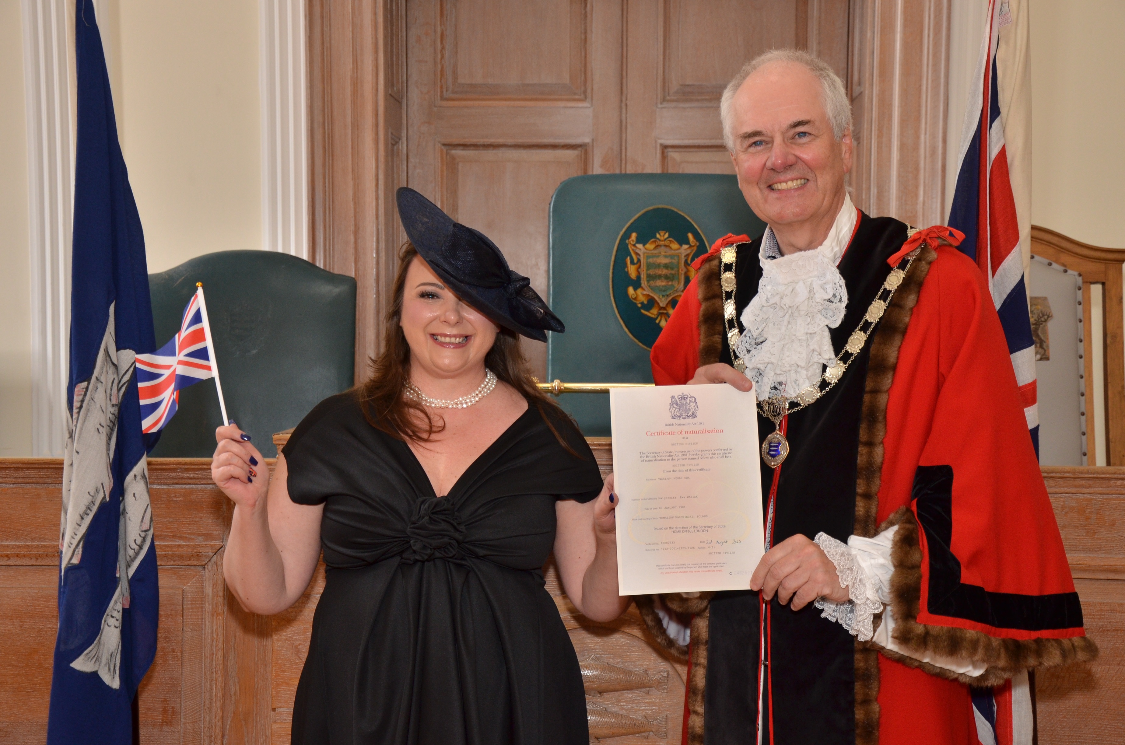 The Mayor presenting a citizenship certificate to a lady wearing a black dress and waving the british flag