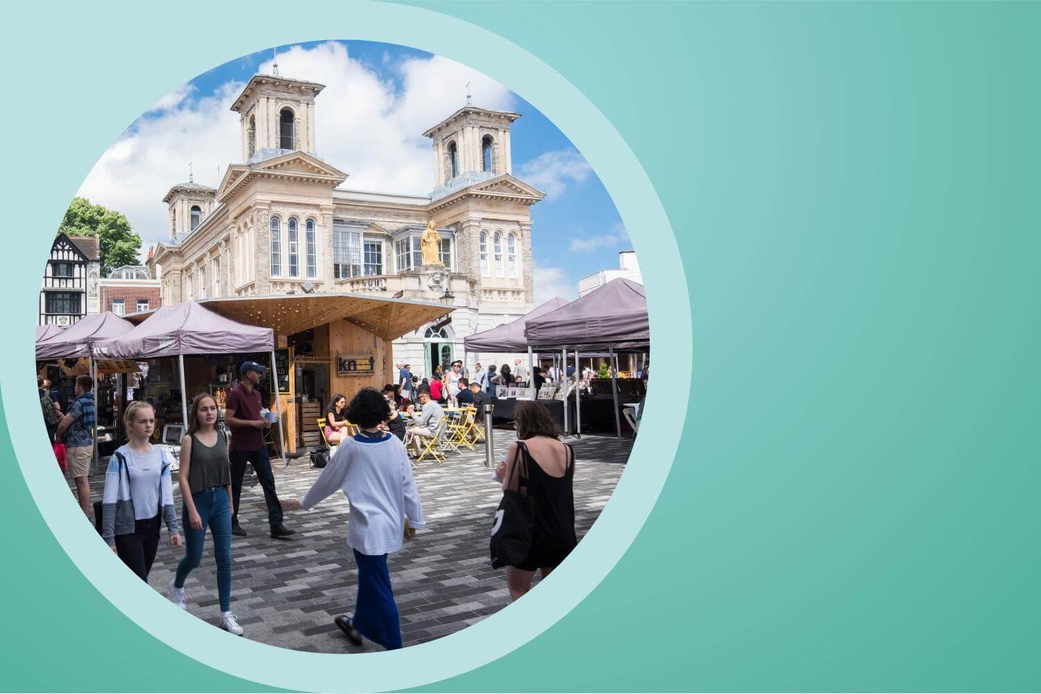 Kingston's Ancient Market Place bustles with activity. People are carrying shopping bags.