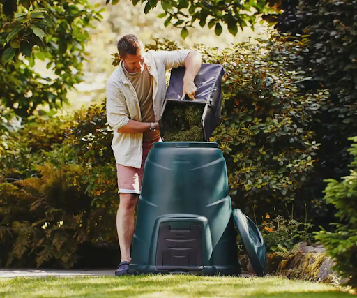 A man in shorts fills up his green compost bin.