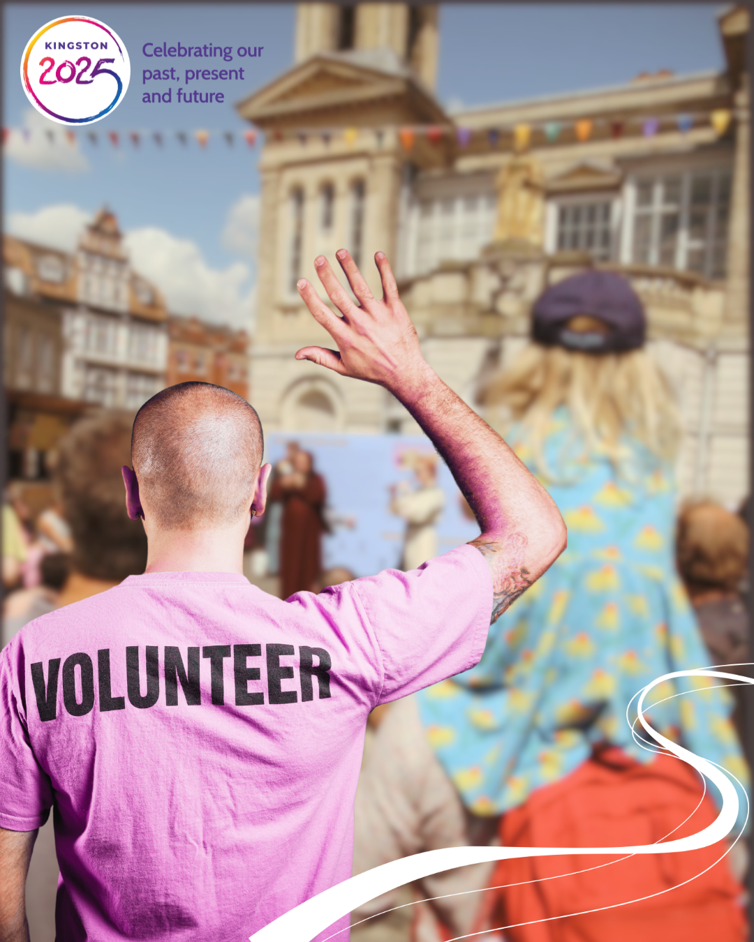 a man in a volunteer T shirt with his hand up is placed in the crowd gathered for a street performance scene in front of the ancient market house