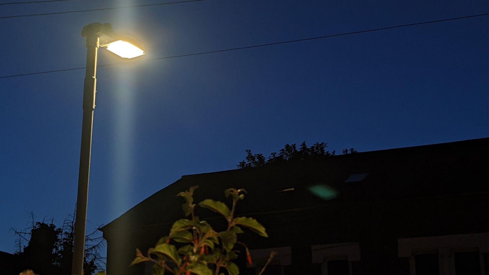 An LED street light shinging on a dark street against a deep blue sky.