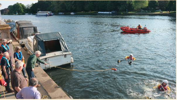 The Royal National Lifeboat Institution (RNLI) providing throwline training to members of the public. Volunteer in the water holding on to a throwline while a trainer holds on to the other end from a river bank. 