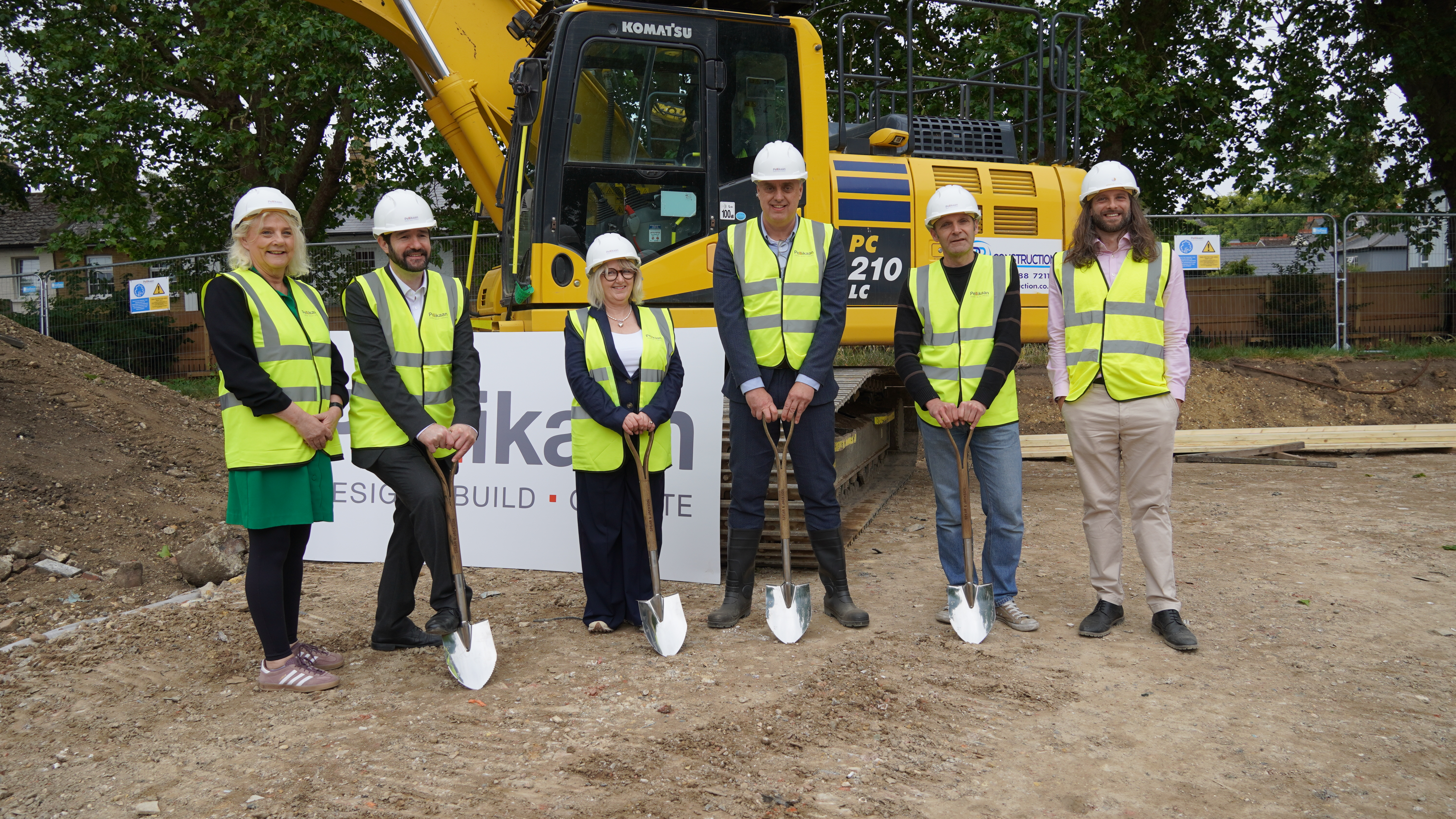 Image showing 6 people holding spades and wearing hard hats and high visibility vests, all standing in front of a piece of construction machinery.