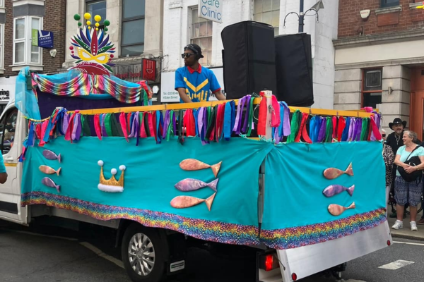 A man plays music from the back of an electric truck. The truck is decorated with fabric in a range of different colours.