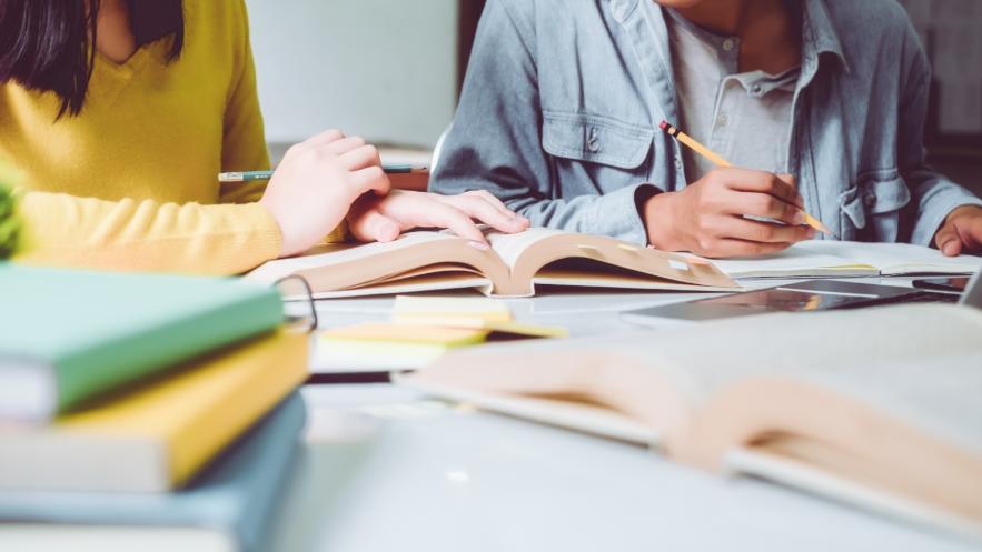Close up of two female students working at a desk covered with books