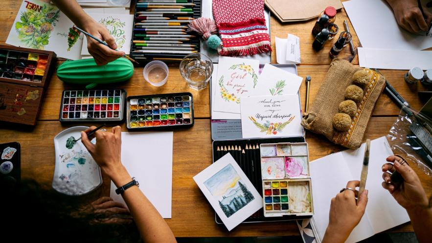 Looking down on a table covered with art materials as people around the table work on individual projects