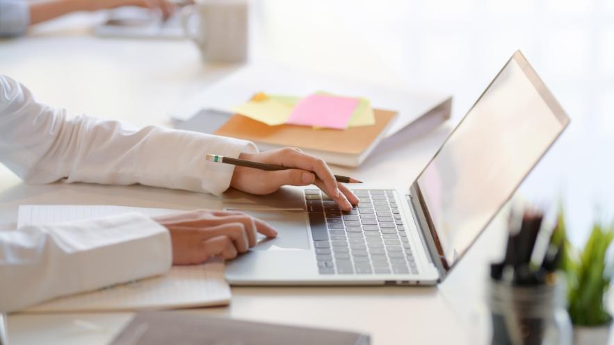 Close up of someone working at a laptop on an office desk. We see only the person's arms as they use the laptop.
