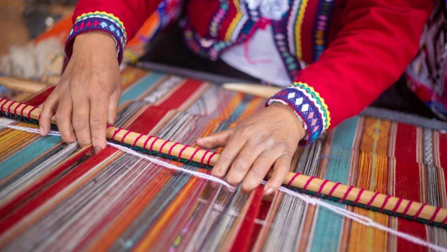 Close up of someone working at a loom. They are producing a multi-coloured striped fabric.