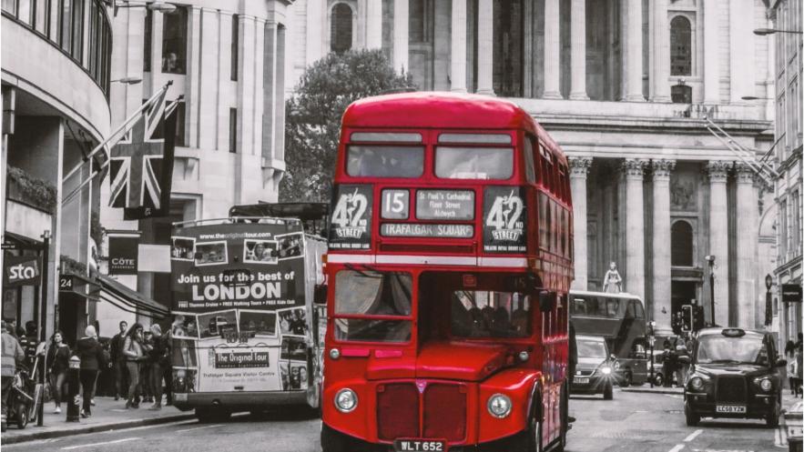 A red London bus moves towards us along a street in the city centre