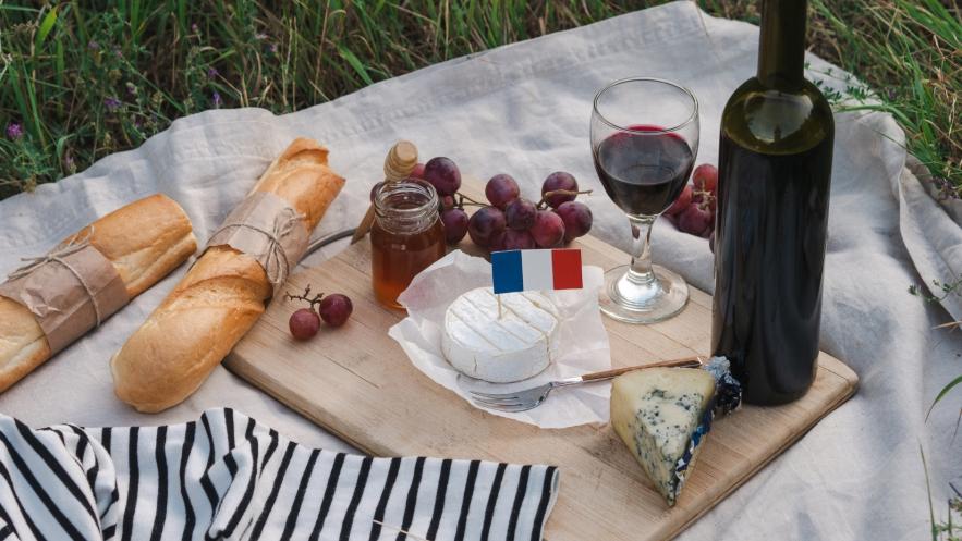 Close up of a picnic with items including wine, cheese, grapes and French sticks