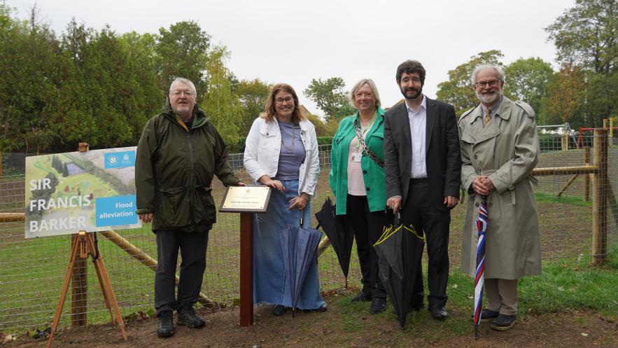 Outdoor scene with sign far left saying Sir Francis Barker Flood Alleviation and four Kingston councillors - left to right - with local resident Bruce Stuart together with plaque to dedicate the new scheme to former councillor Christine Stuart